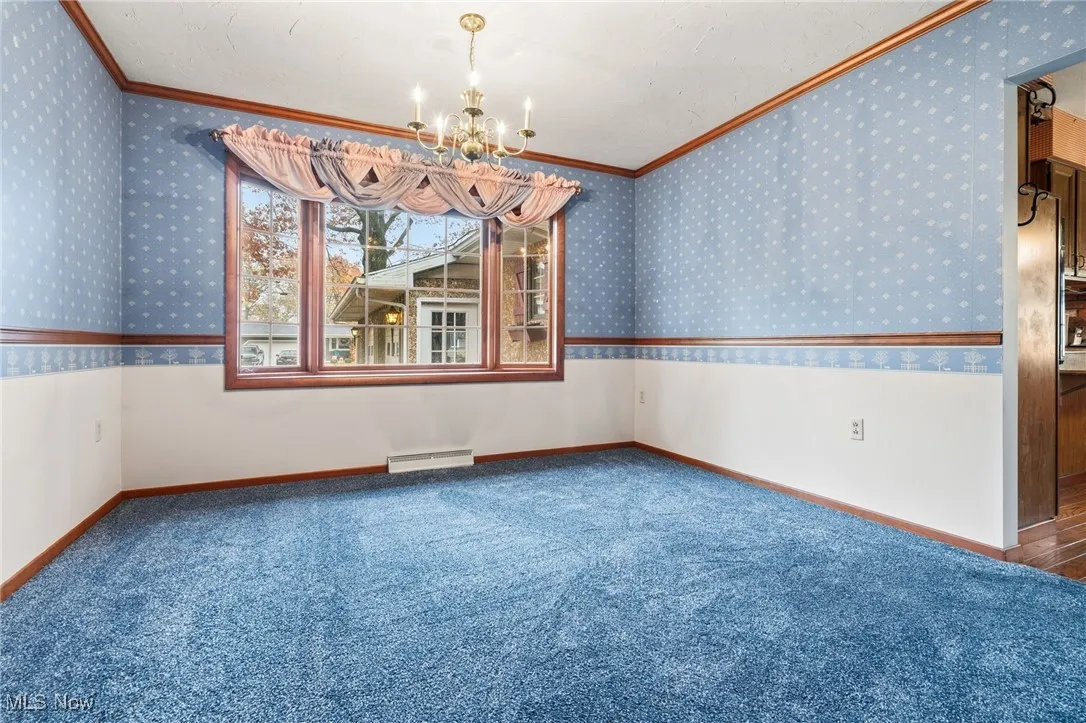 Carpeted dining room with ornamental molding, a chandelier, and a wainscoted wall