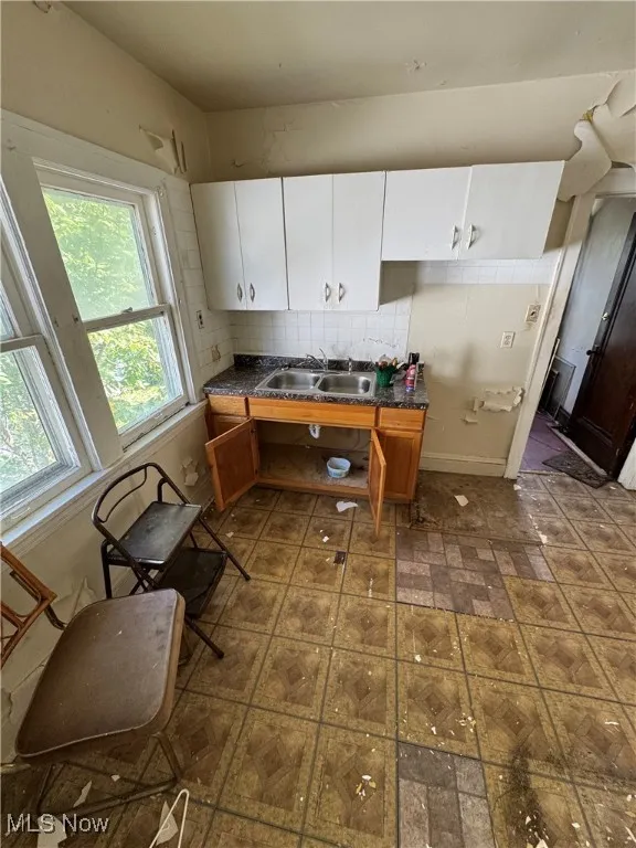 Kitchen with white cabinetry, dark countertops, brown cabinets, and decorative backsplash