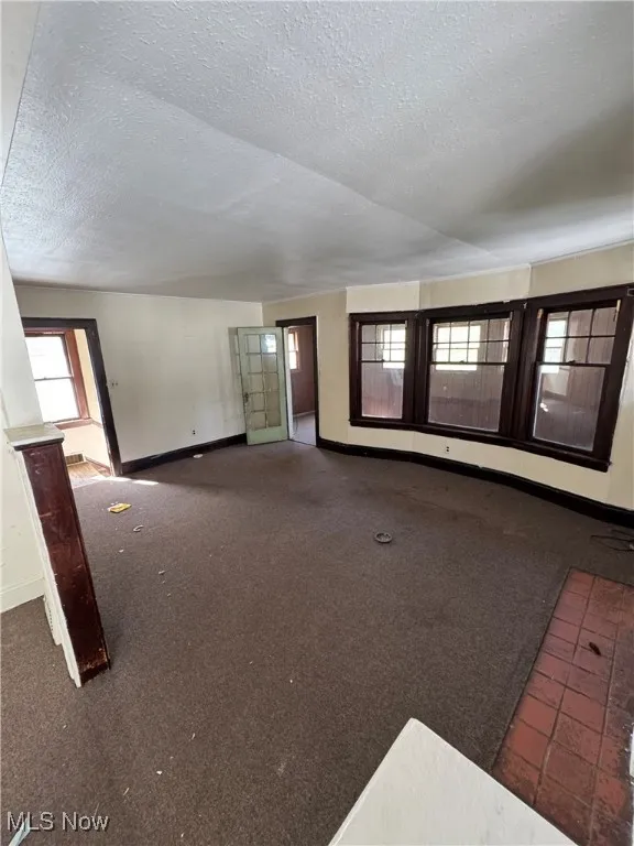 Unfurnished living room with a textured ceiling and dark carpet