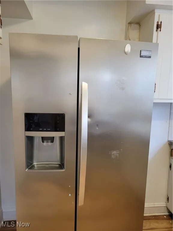 Kitchen view of stainless steel fridge with ice dispenser, white cabinets, and wood finished floors