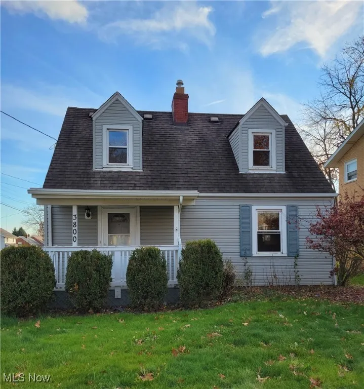 Cape cod home featuring a porch, a chimney, a front yard, and a shingled roof