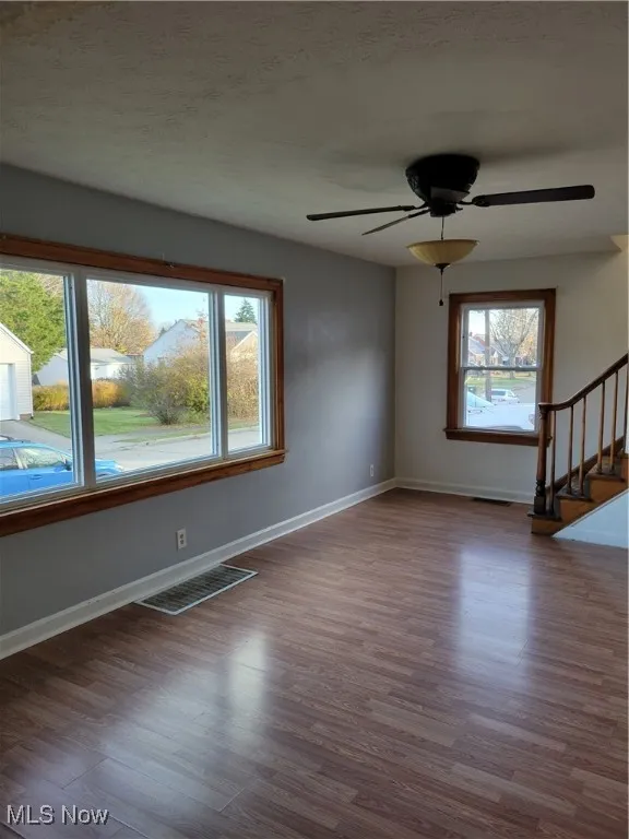 Spare room featuring stairs, dark wood-style floors, ceiling fan, and healthy amount of natural light