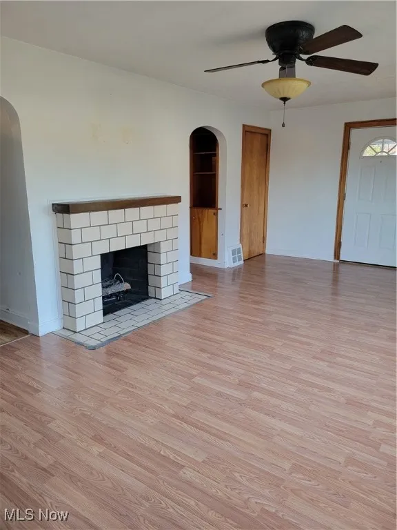 Unfurnished living room featuring arched walkways, a fireplace, light wood-style flooring, and a ceiling fan