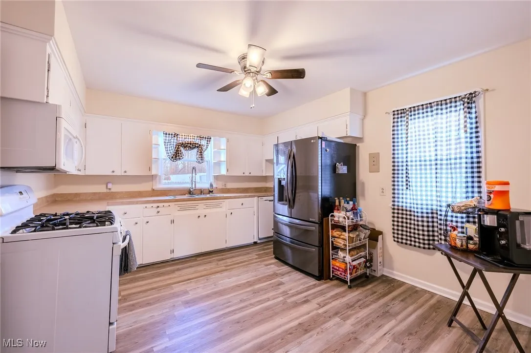 Kitchen featuring white appliances, light countertops, white cabinets, light wood-style flooring, and ceiling fan
