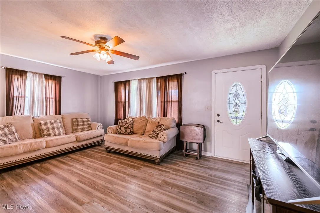 Living area with a textured ceiling, wood finished floors, healthy amount of natural light, and ceiling fan
