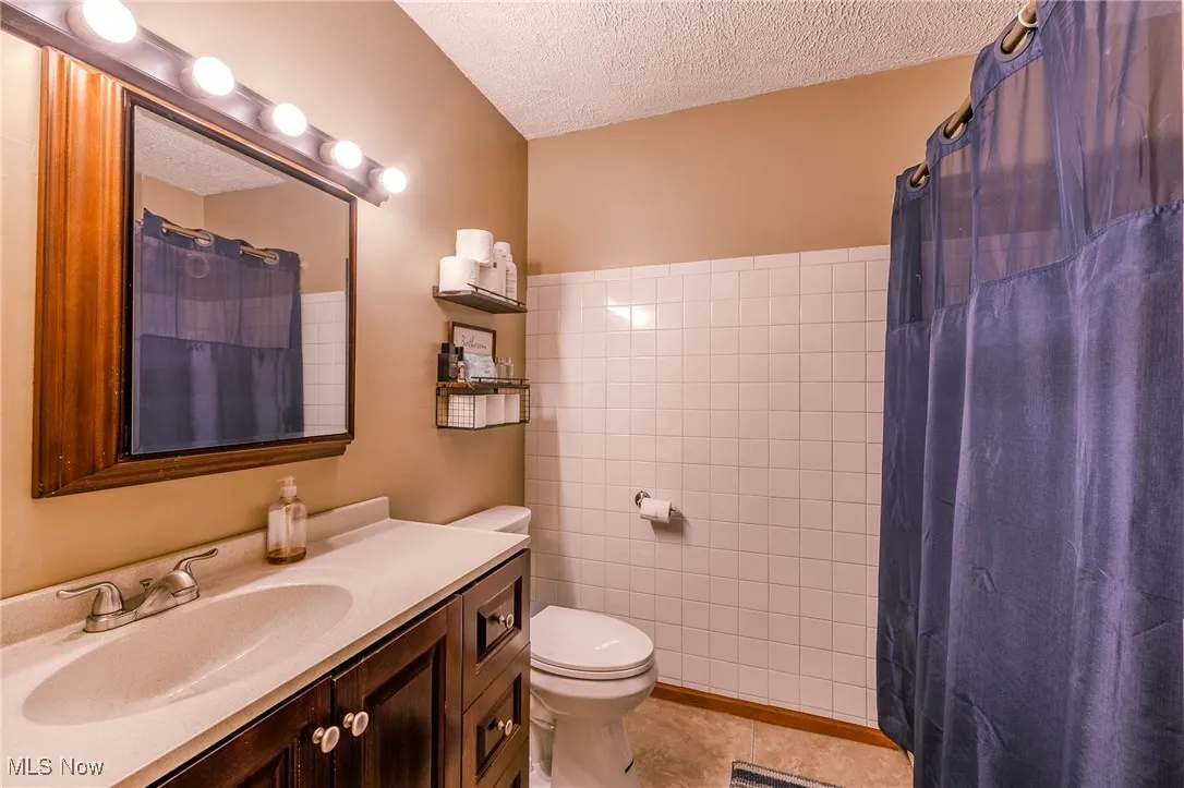 Full bath featuring a textured ceiling, vanity, a shower with shower curtain, and light tile patterned floors