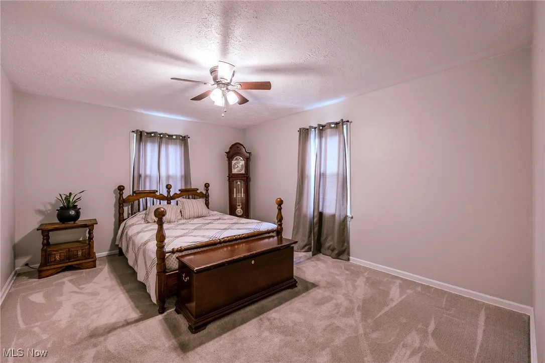 Bedroom with a textured ceiling, light carpet, and ceiling fan