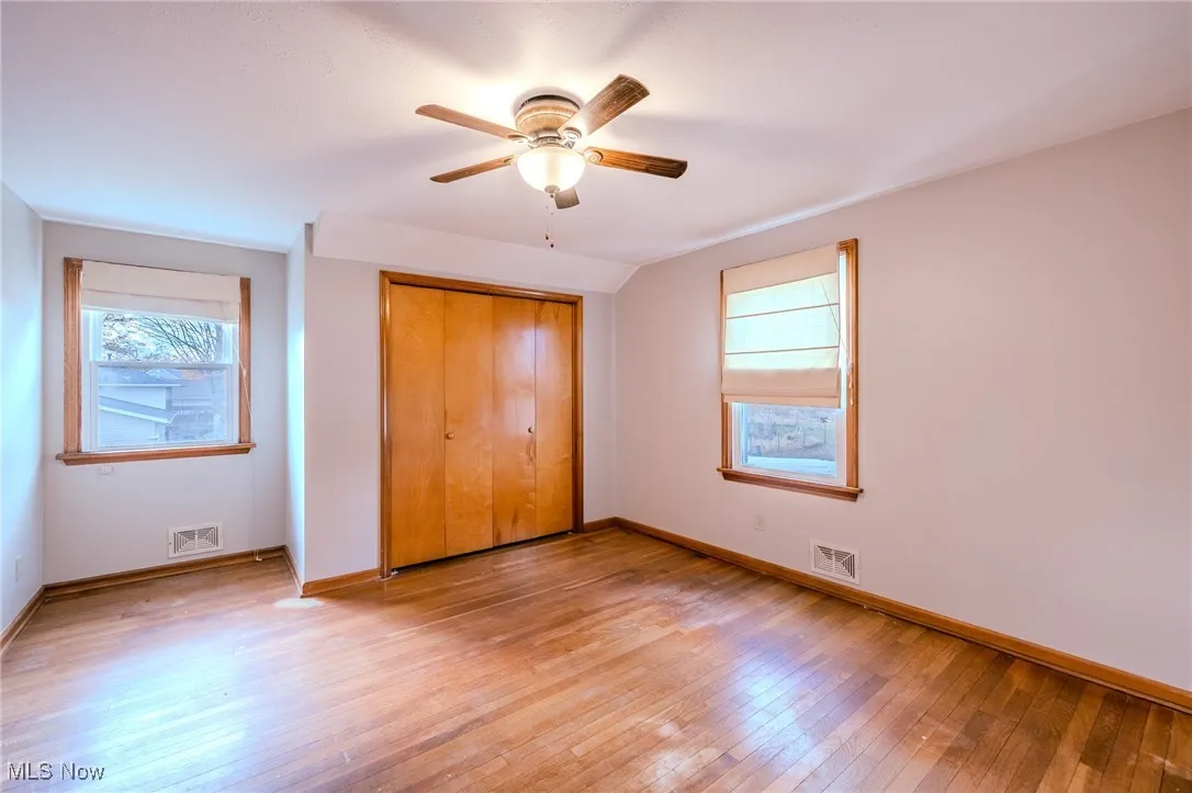 Unfurnished bedroom with light wood-style floors, ceiling fan, multiple windows, a closet, and lofted ceiling
