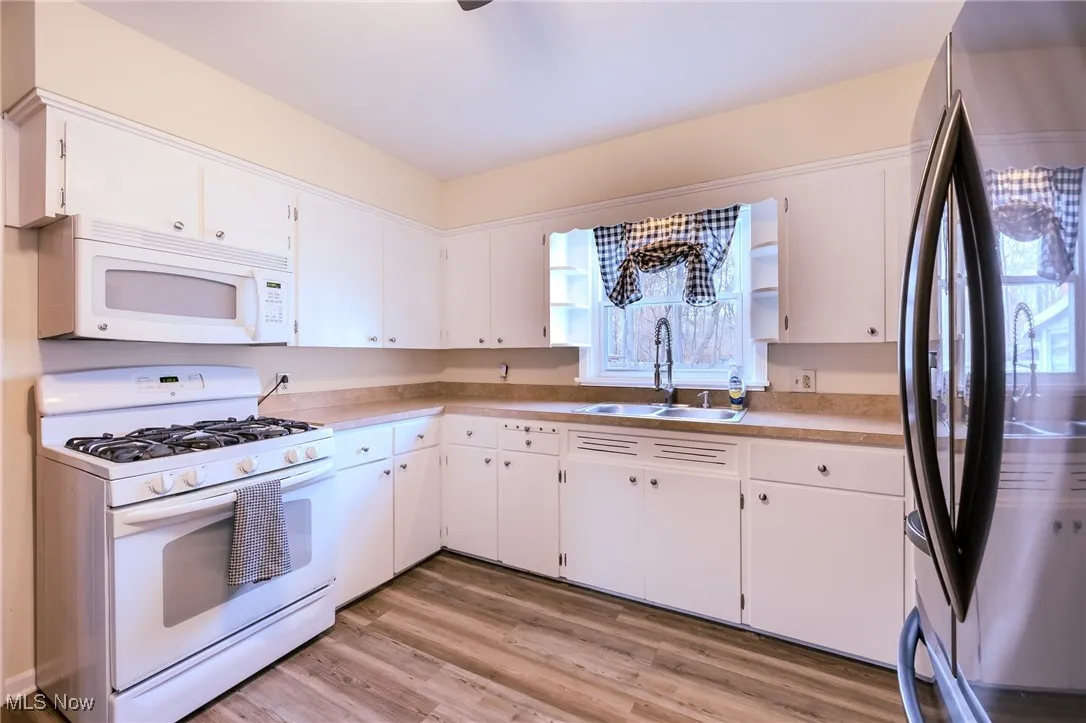 Kitchen with white appliances, light countertops, light wood-style floors, and white cabinets