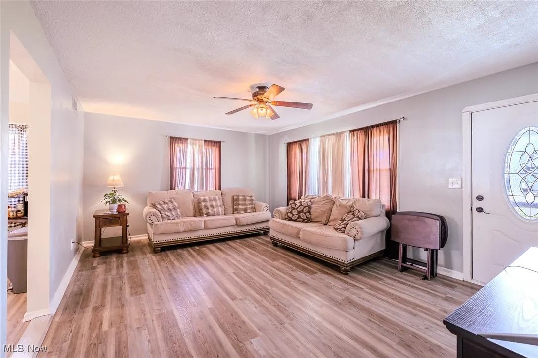 Living room with ceiling fan, light wood finished floors, and a textured ceiling