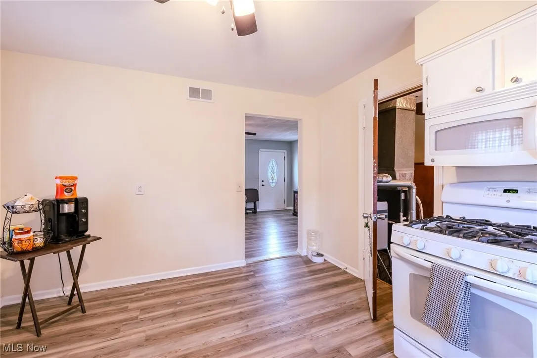 Kitchen featuring white appliances, light wood-style floors, ceiling fan, and white cabinetry