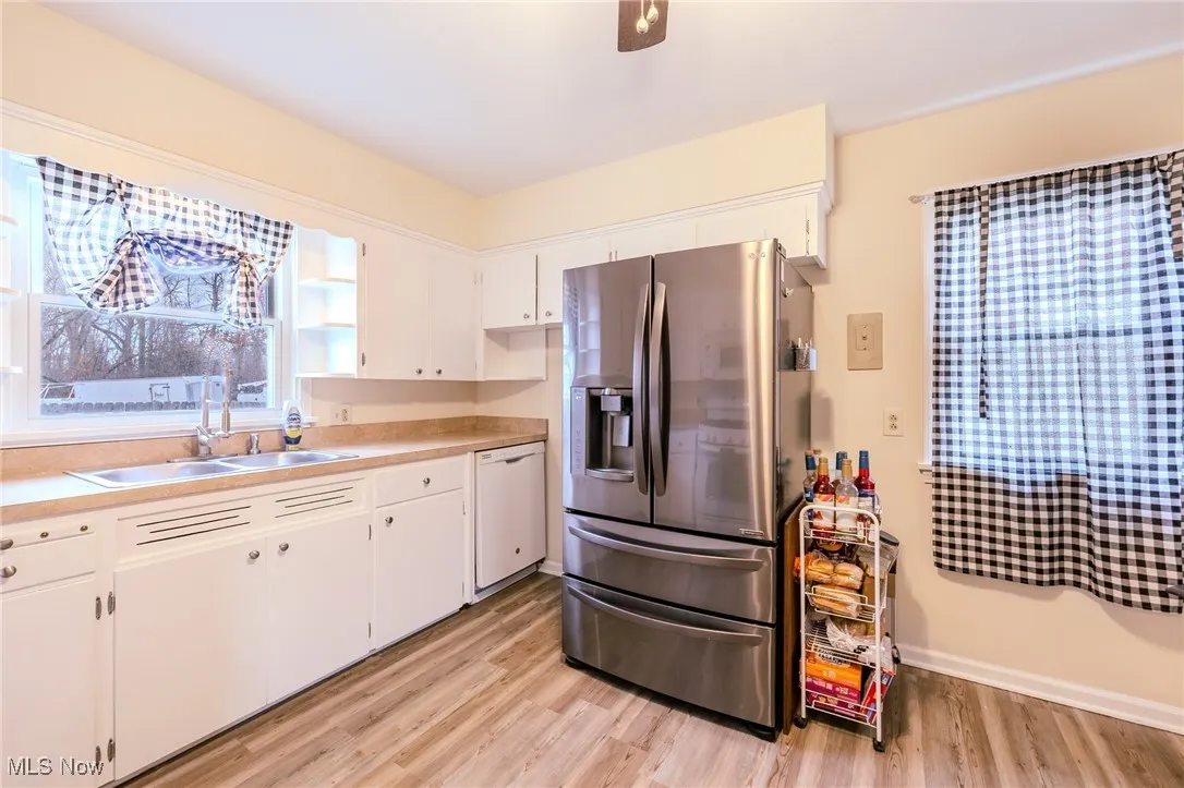Kitchen with stainless steel fridge with ice dispenser, light countertops, white dishwasher, white cabinetry, and light wood-style floors