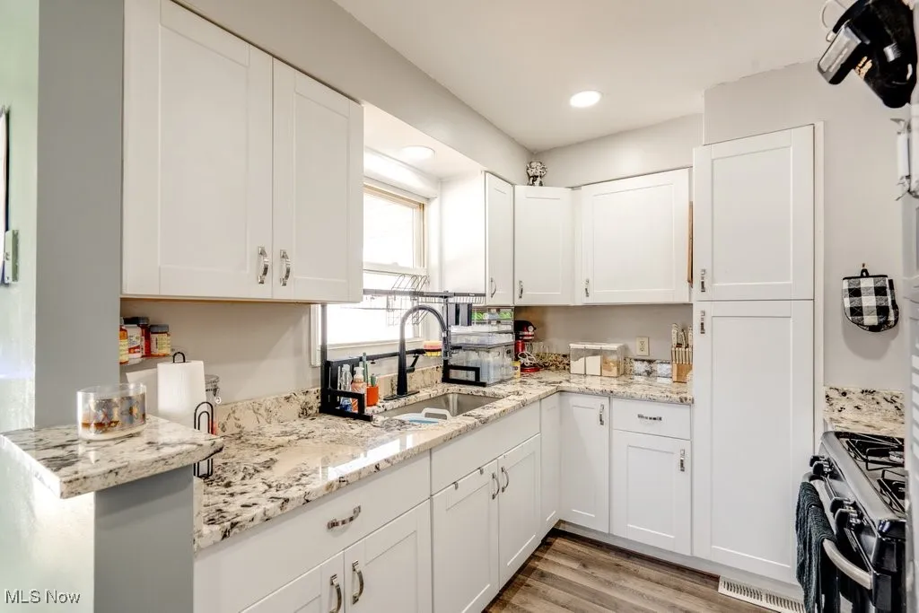 Kitchen with range with gas stovetop, white cabinets, light stone countertops, light wood-style floors, and recessed lighting