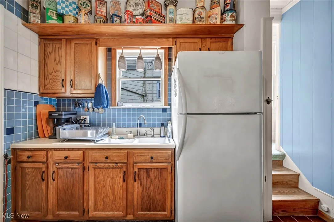 Kitchen with freestanding refrigerator, brown cabinets, light countertops, decorative backsplash, and wood finished floors