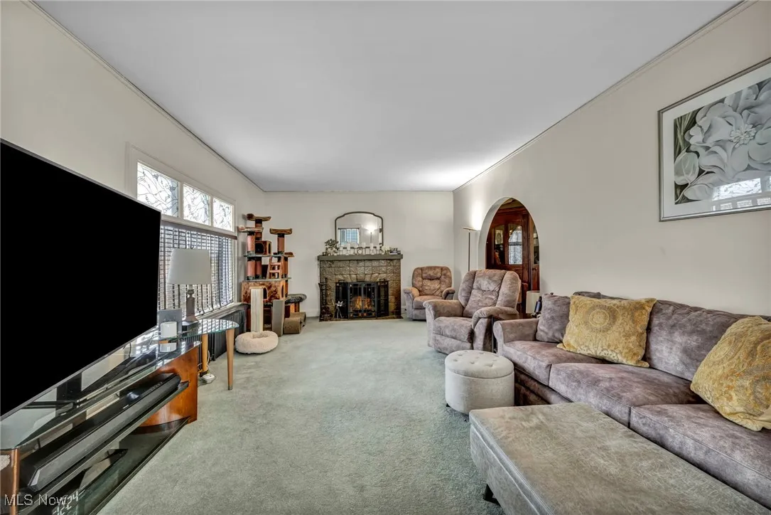 Carpeted living room featuring crown molding, a fireplace, and arched walkways