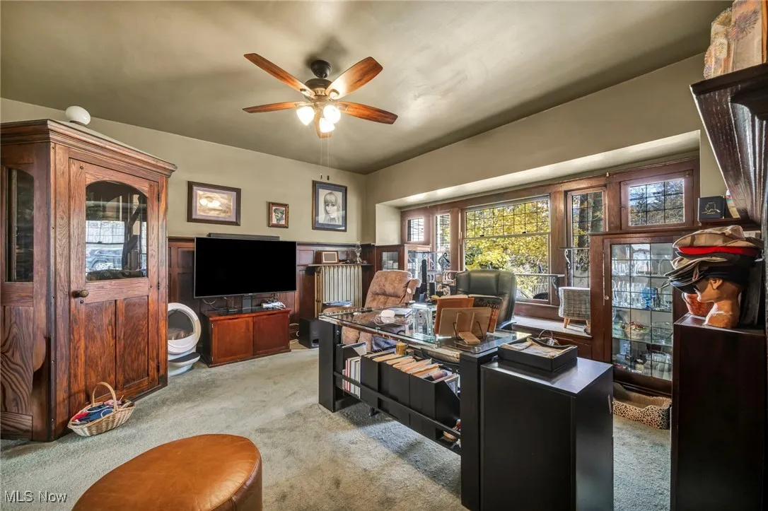 Living area with an office area, light carpet, wainscoting, and a ceiling fan