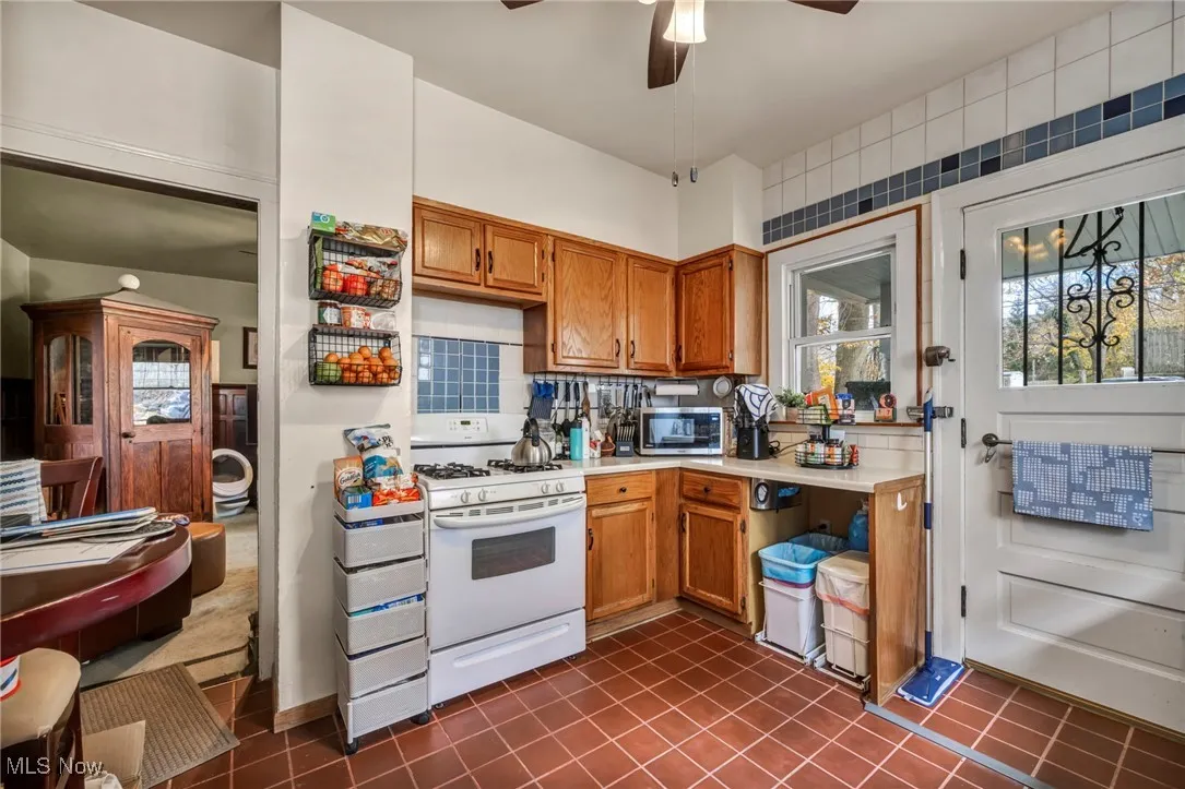 Kitchen with light countertops, brown cabinets, white range with gas stovetop, stainless steel microwave, and dark tile patterned floors