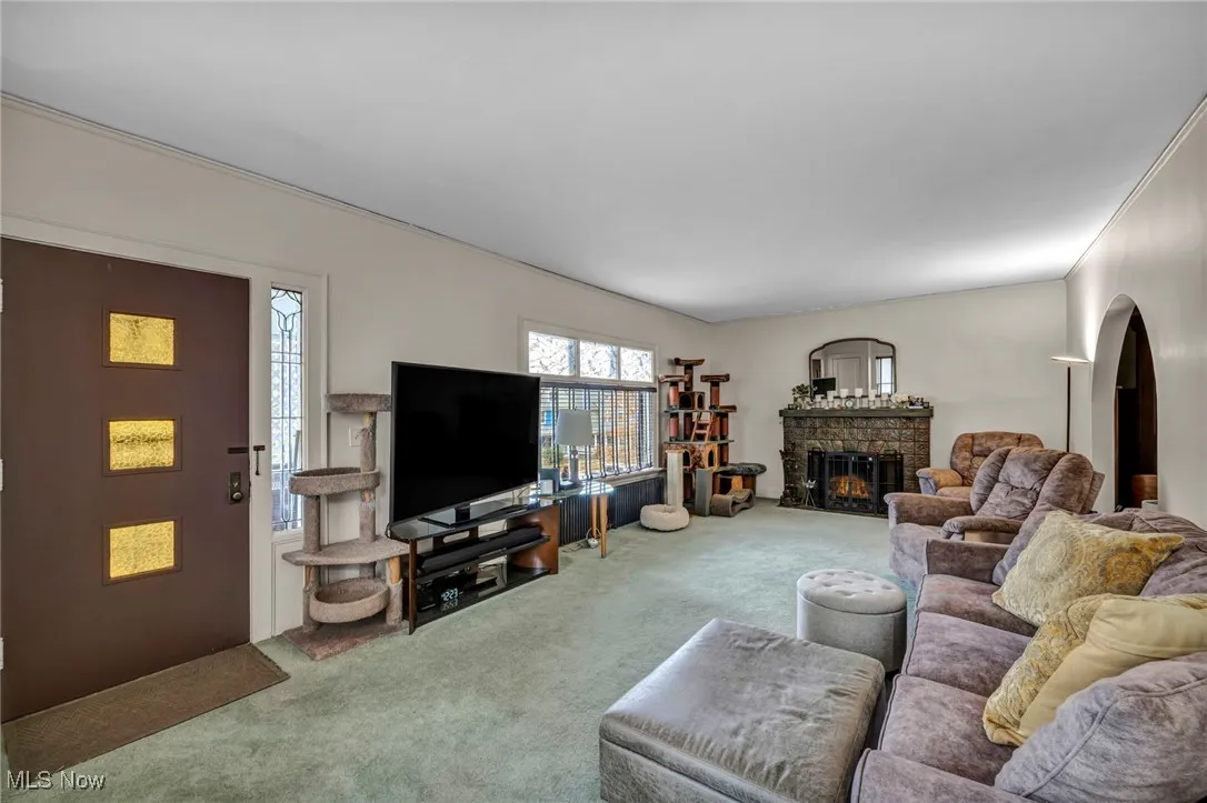 Living room with a brick fireplace, carpet flooring, and crown molding