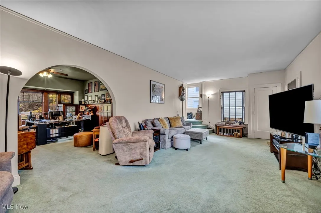 Carpeted living room featuring a ceiling fan, an office area, and arched walkways