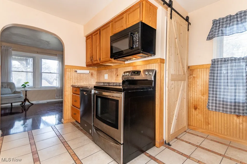 Stainless steel range, built-in microwave, and dishwasher with barn door to side entrance and basement