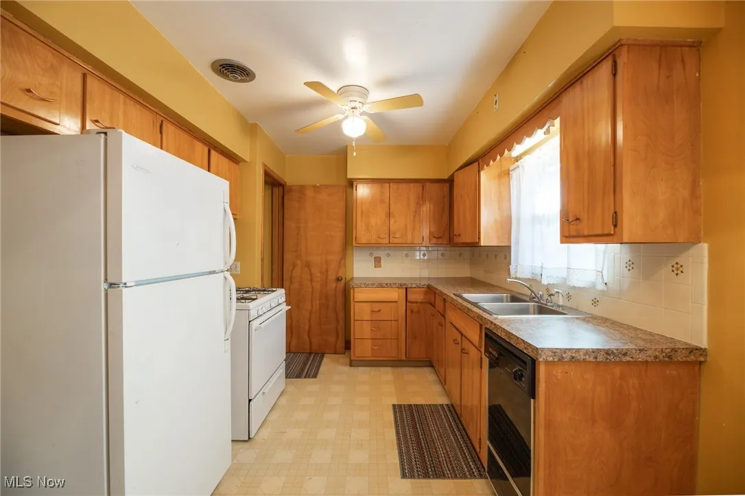 Kitchen with white appliances, light flooring, brown cabinetry, backsplash, and a ceiling fan
