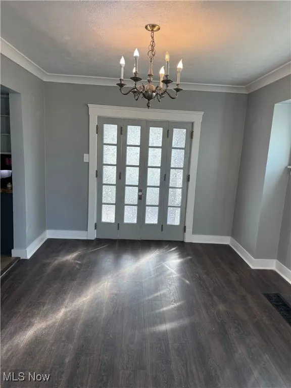 Unfurnished dining area with crown molding, dark wood finished floors, a chandelier, and a textured ceiling