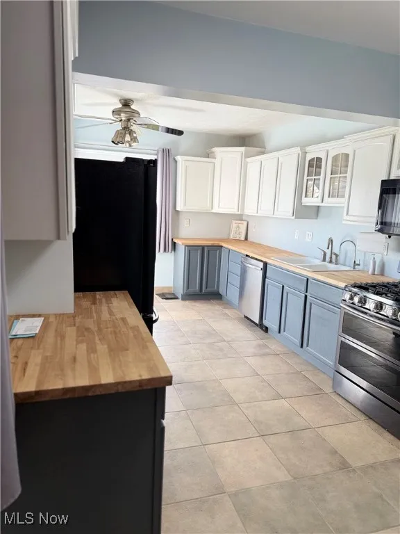 Kitchen with butcher block countertops, stainless steel appliances, glass insert cabinets, white cabinetry, and gray cabinetry