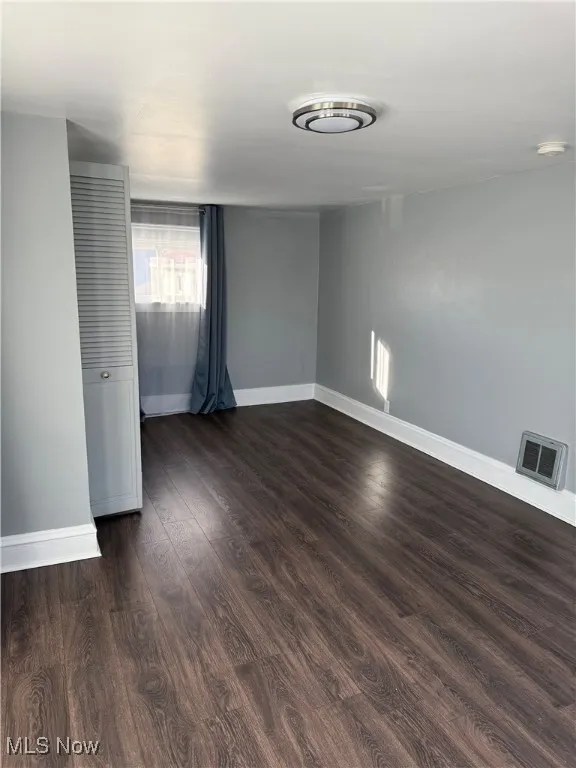 Unfurnished room with baseboards and dark wood-type flooring
