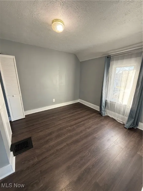 Empty room with a textured ceiling, dark wood-style floors, and vaulted ceiling