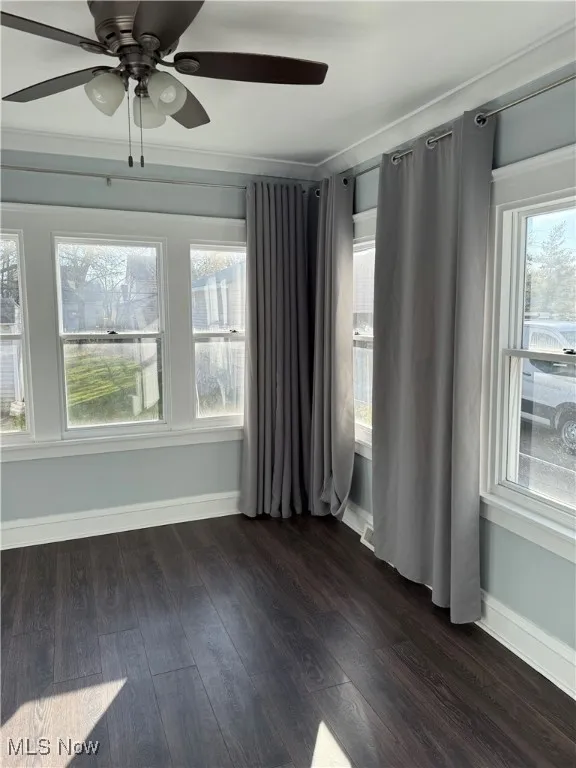 Spare room featuring ceiling fan, healthy amount of natural light, dark wood finished floors, and crown molding