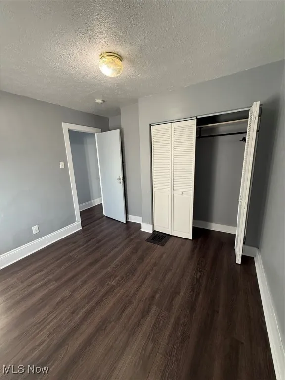 Unfurnished bedroom with a textured ceiling, a closet, and dark wood-style flooring