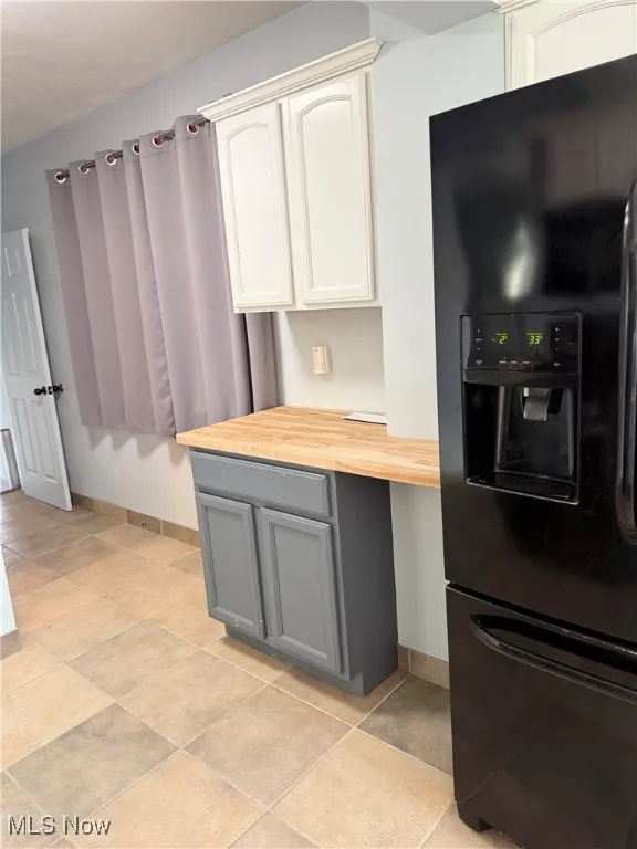 Kitchen featuring butcher block countertops, black fridge with ice dispenser, gray cabinetry, white cabinets, and light tile patterned flooring