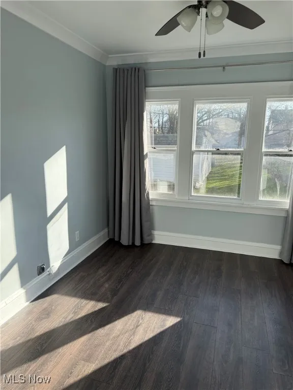 Empty room with ornamental molding, dark wood-type flooring, and ceiling fan