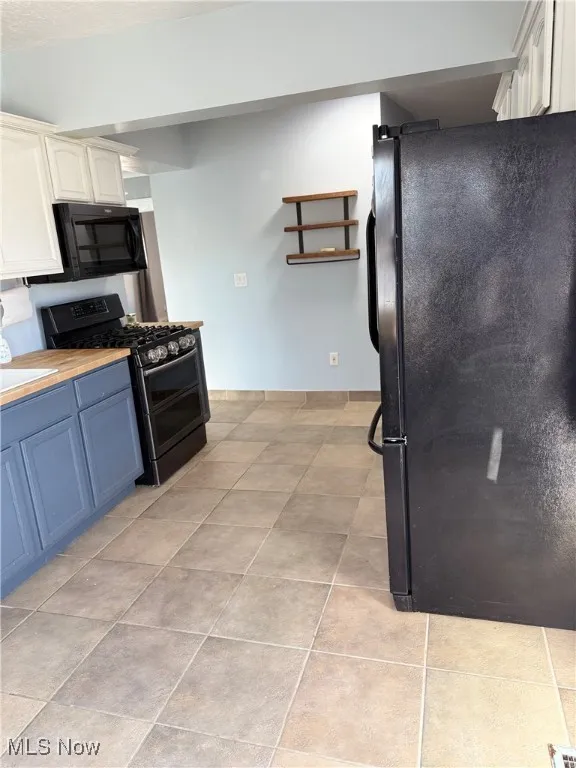 Kitchen with black appliances, wood counters, white cabinetry, light tile patterned flooring, and blue cabinets