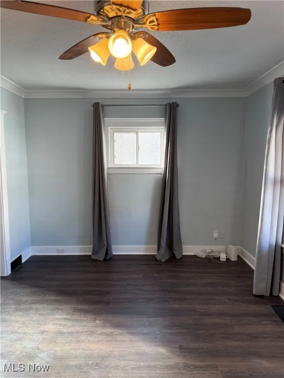 Empty room with a ceiling fan, dark wood-style flooring, ornamental molding, and a textured ceiling
