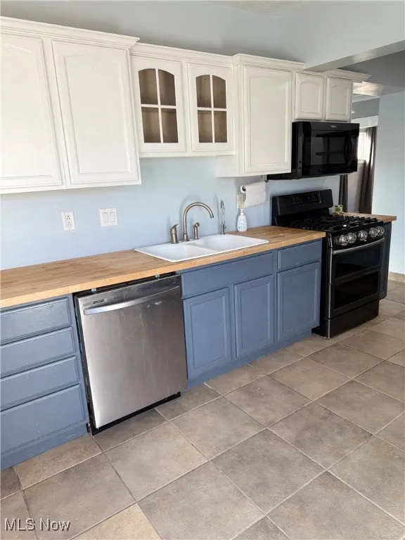 Kitchen with wooden counters, double oven range, glass insert cabinets, stainless steel dishwasher, and white cabinets