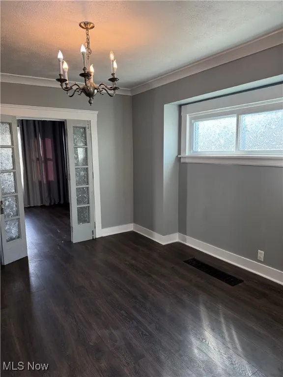 Empty room with a chandelier, dark wood-style flooring, a textured ceiling, and ornamental molding