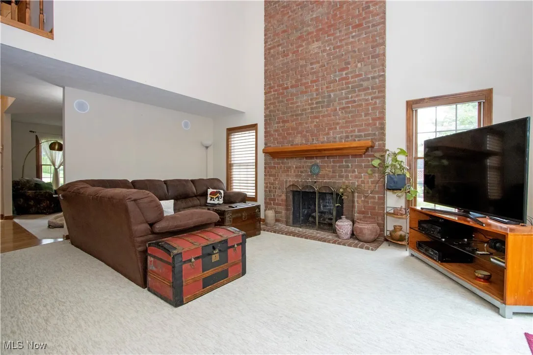 Living area with a high ceiling, carpet flooring, a brick fireplace, and healthy amount of natural light