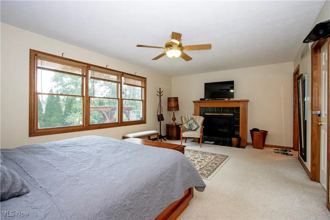 Bedroom with a tile fireplace, carpet floors, and a ceiling fan