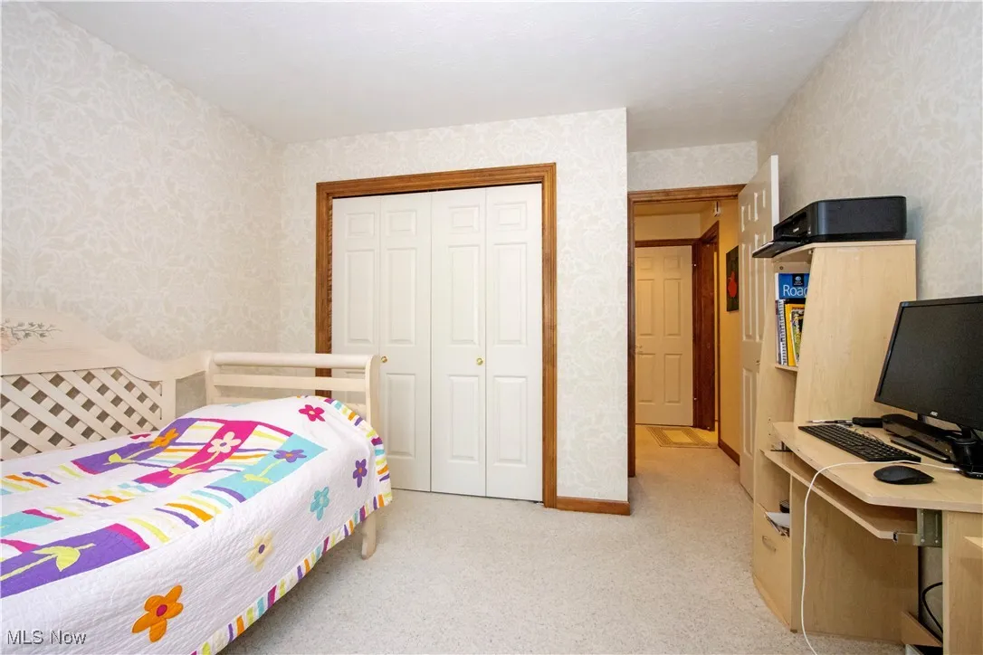 Bedroom featuring wallpapered walls, light colored carpet, and a closet