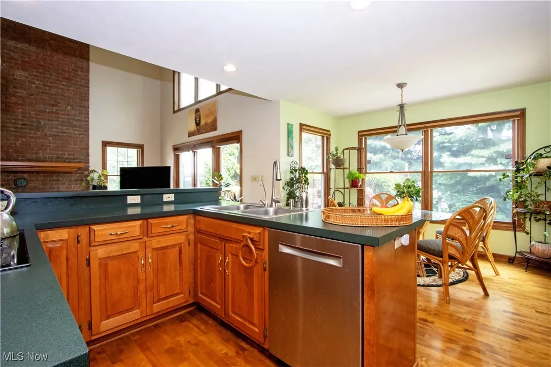 Kitchen featuring dishwasher, wood finished floors, dark countertops, brown cabinets, and hanging light fixtures