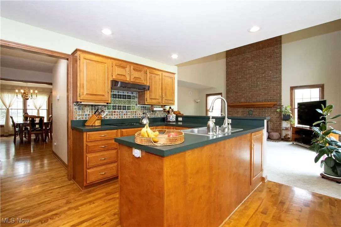 Kitchen featuring under cabinet range hood, dark countertops, a chandelier, light wood-style flooring, and backsplash