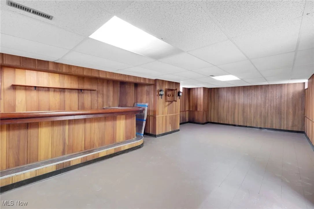 Bar with wooden walls, light floors, brown cabinets, and a drop ceiling