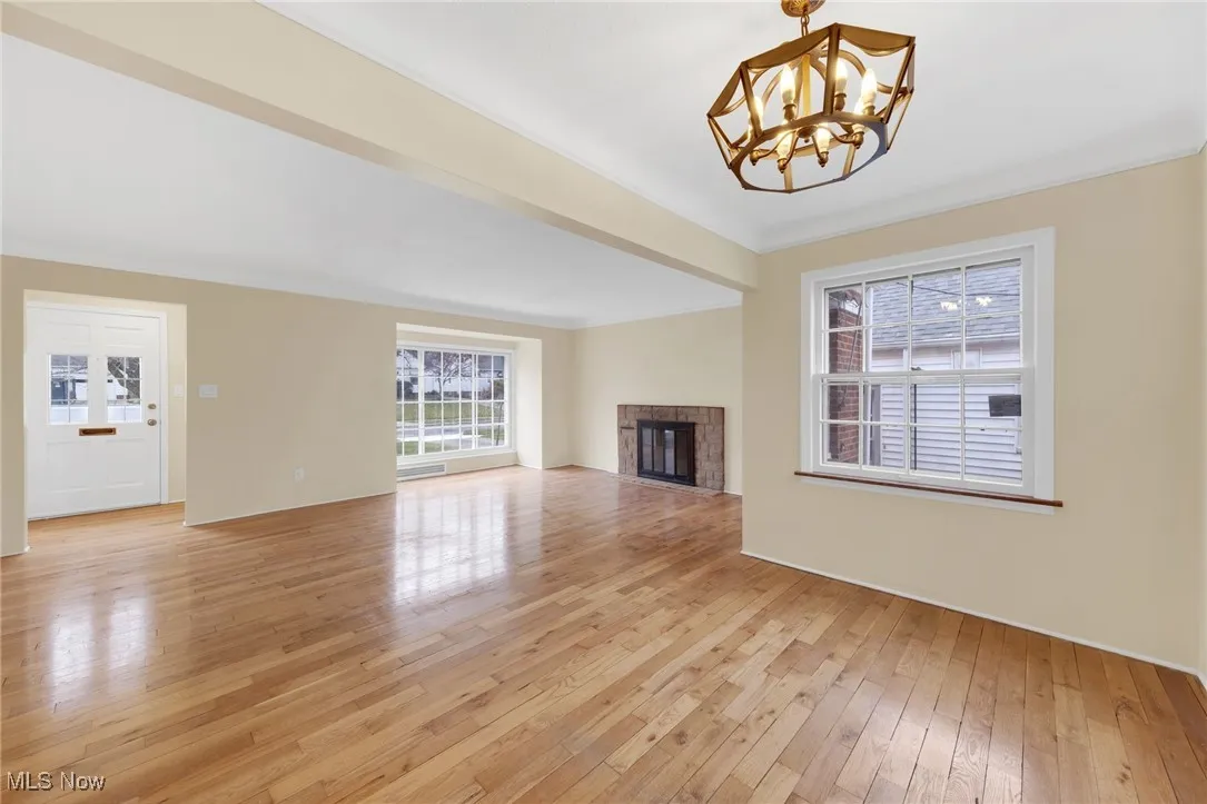 Unfurnished living room with a brick fireplace, light wood finished floors, a chandelier, and ornamental molding