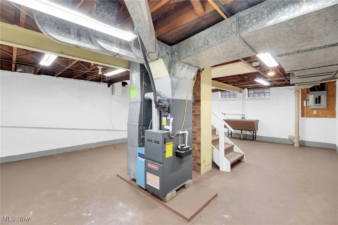 Unfinished basement featuring electric panel, stairs, and heating unit