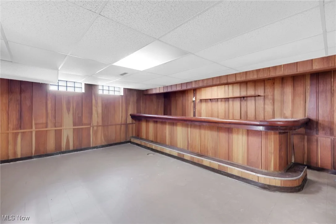 Bar with wood walls, a paneled ceiling, brown cabinets, and tile patterned floors