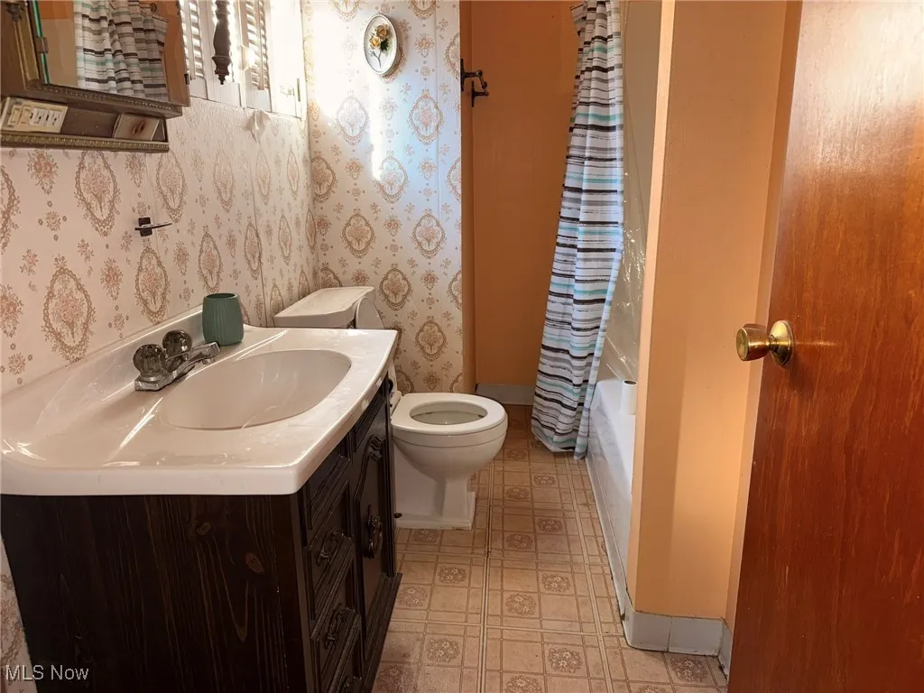 Bathroom with vanity, shower / tub combo, wallpapered walls, and light flooring