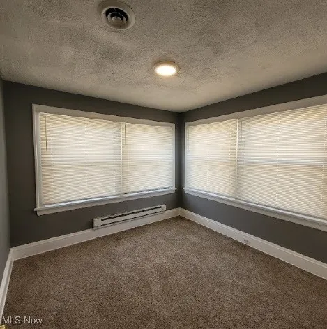 Empty room featuring a textured ceiling, dark colored carpet, and a baseboard radiator