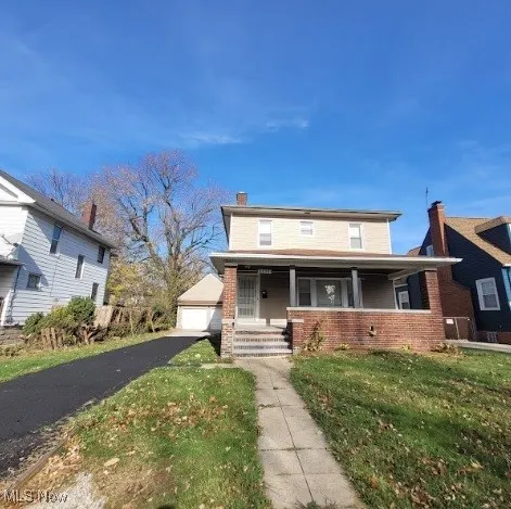View of front facade with covered porch, a chimney, brick siding, a front lawn, and a garage
