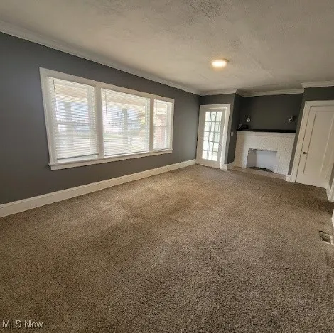 Unfurnished living room featuring carpet floors, crown molding, a textured ceiling, and a fireplace